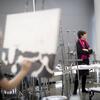 student painting, two people talk behind her canvas