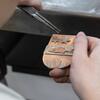 Student holding a small metal piece of work. In her other hand she holds tweezers to the metal.
