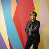 Susan Cahan stands in front of a multicolored wall with her arms crossed, smiling at the camera.