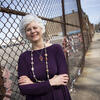 Lisa Kay leans against a fence, smiling warmly at the camera and crossing her arms.