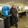 Kelly Holohan leans against a table in a Tyler design studio, smiling at the camera.