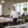 Christopher McAdams standing in an architecture studio, looking at and smiling for the camera.