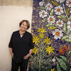 Sally Harrison smiles at the camera, standing in front of a vibrant mural filled with flowers.