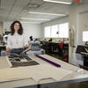 Mia Culberston stands in a Tyler design studio, holding a book in her hands and smiling at the camera.