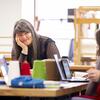 A professor smiles and looks at someone while both are seated at a table, engaged in a friendly and thoughtful conversation.