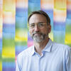  John Hatfield's headshot, looking at the camera with a rainbow-colored wall behind him.