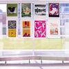 Graphic design posters are hung up on large windows in a hallway, creating an eye-catching display. The vibrant designs are clearly visible through the glass, adding a creative touch to the space while allowing natural light to filter through.