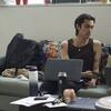 Two students sitting on a couch with their laptops open, talking to eachother.