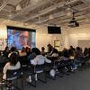 A crowd of people sat, listening to a presentation.