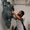 A graduate student adjusting a teal sculptural piece mounted on the wall.