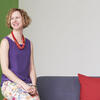 Mariola Alvarez sits on a chair inside Tyler School of Art & Architecture, smiling and looking away from the camera.