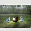 A photo depicting two women sitting on either side of an old TV set in the middle of a green field.