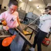 Two people work together at the bench in the glass studio