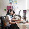 Student wearing headphones sits at a desk, focused on working on a Mac.