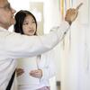 A professor and student are engaged in a class critique, discussing work hanging on the wall. The professor points to a specific piece, while the student listens attentively, holding her notebook and taking notes.