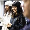 A girl with bangs smiles in the foreground, while another girl stands behind her. Both are gazing off to the left.