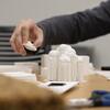 a hand is next to a small 3-d printed model of a building