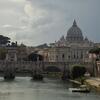 The Tiber River in Rome with a bridge crossing over it. On the right, a street is lined with trees, and in the background, behind the bridge, the Vatican can be seen.