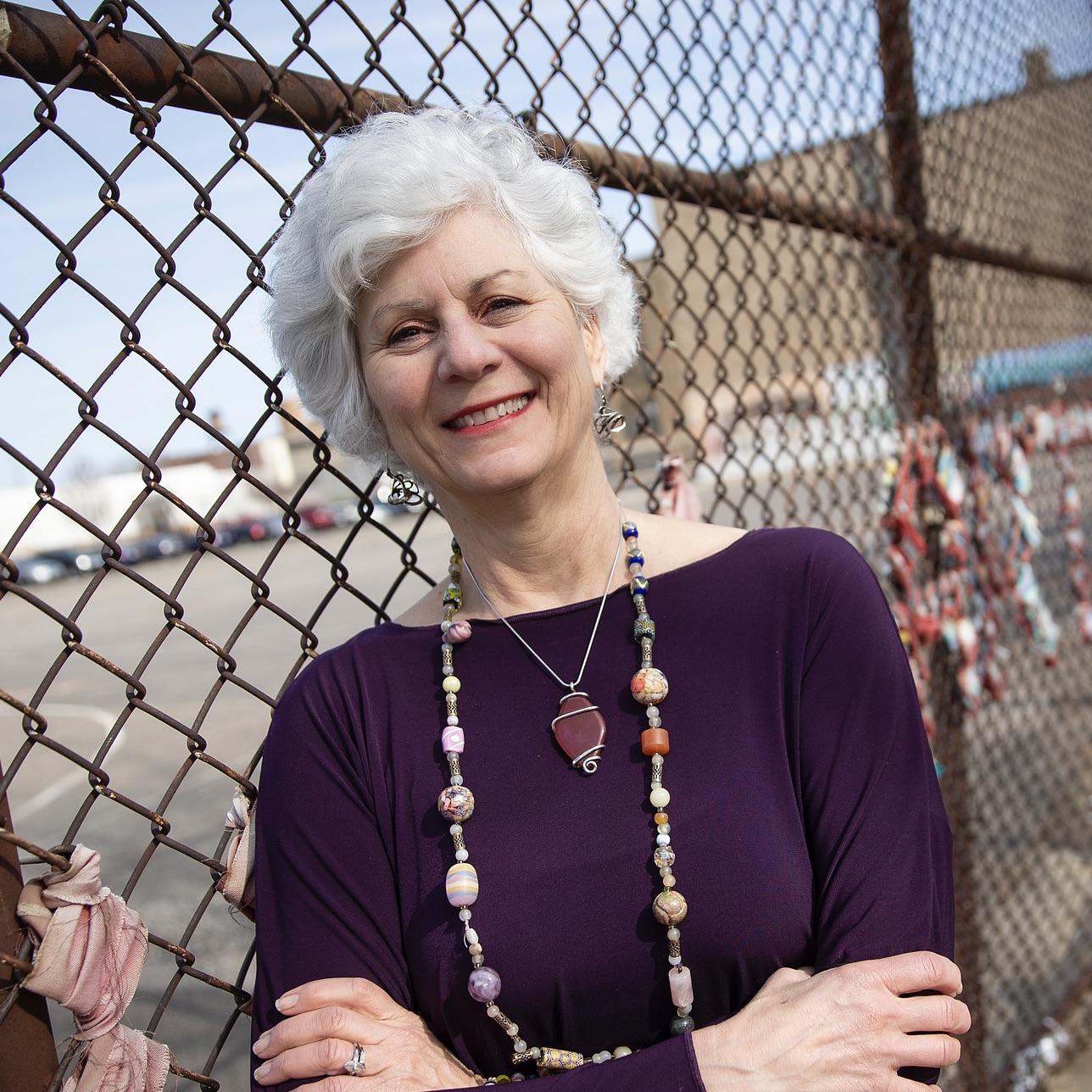 Lisa Kay leans against a fence, smiling warmly at the camera and crossing her arms.