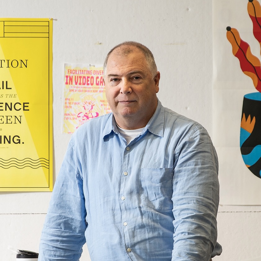  Dave MacCormack, wearing a blue shirt, stands in a design studio at Tyler, looking at the camera.