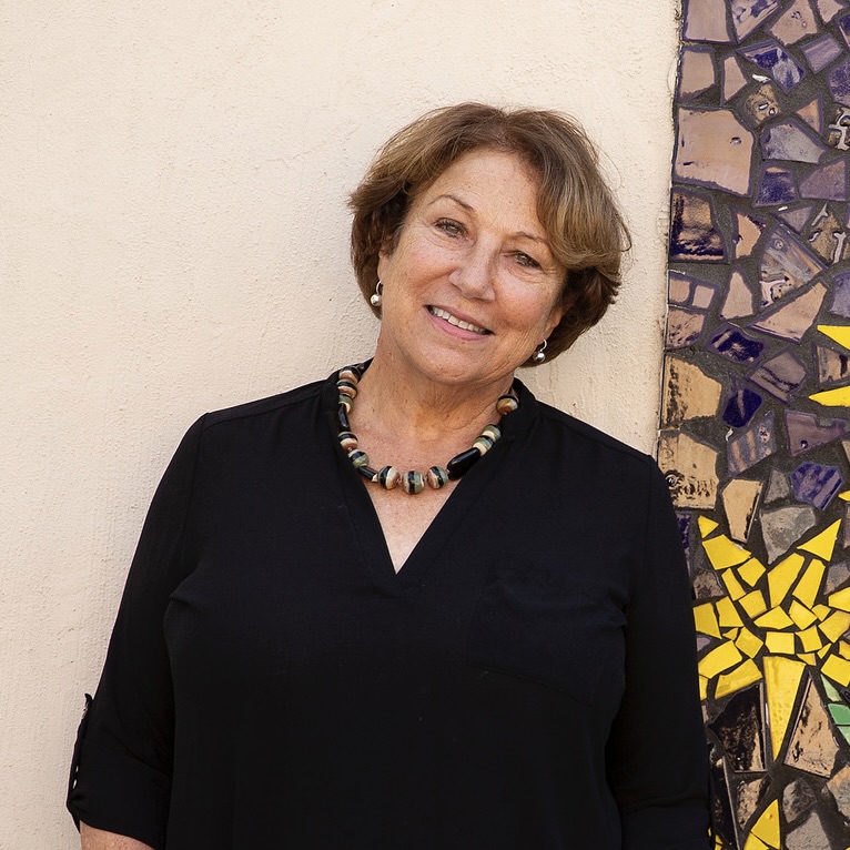 Sally Harrison smiles at the camera, standing in front of a vibrant mural filled with flowers.