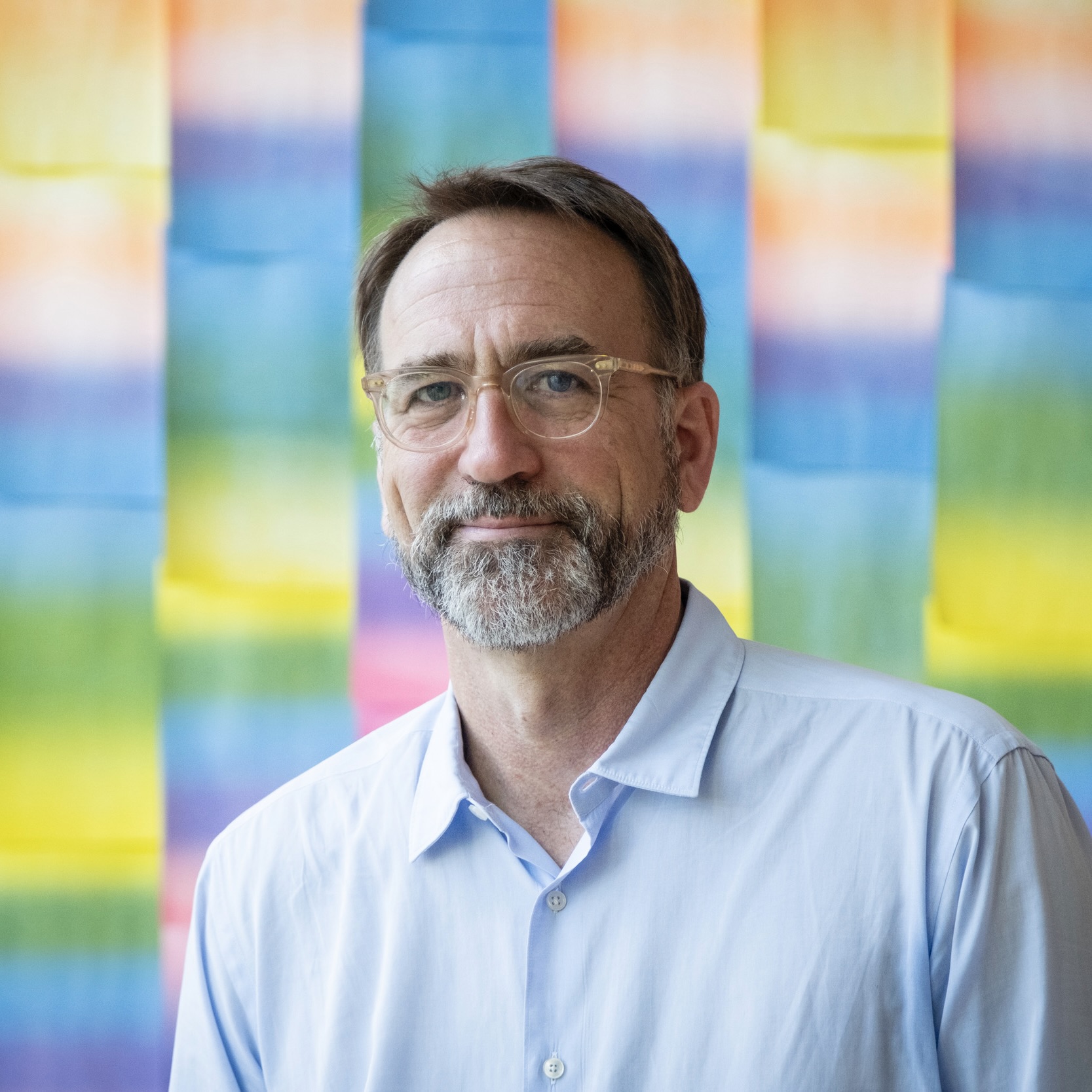  John Hatfield looking at the camera with a rainbow-colored wall behind him.