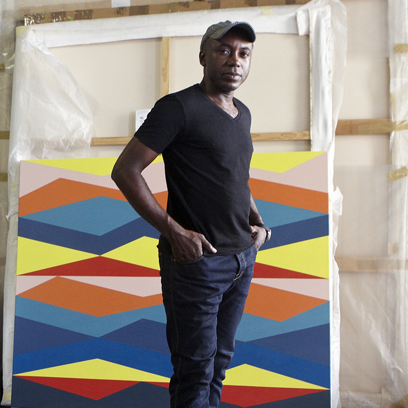 Odili Donald Odita stands in front of a colorful painting looking at the camera