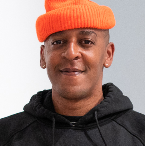 Close-up portrait of a person wearing a neon orange beanie and a black hoodie.